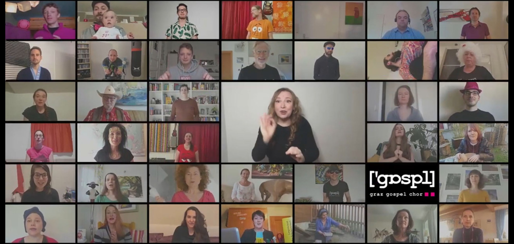 Ein Screenshot eines Videoanrufs mit einer Liste verschiedener Teilnehmer, die an eine Probe des Grazer Gospelchors erinnert. Eine Person in der Mitte gestikuliert mit den Händen, möglicherweise mit Gebärden. Im Hintergrund sind verschiedene Haushaltssituationen zu sehen.